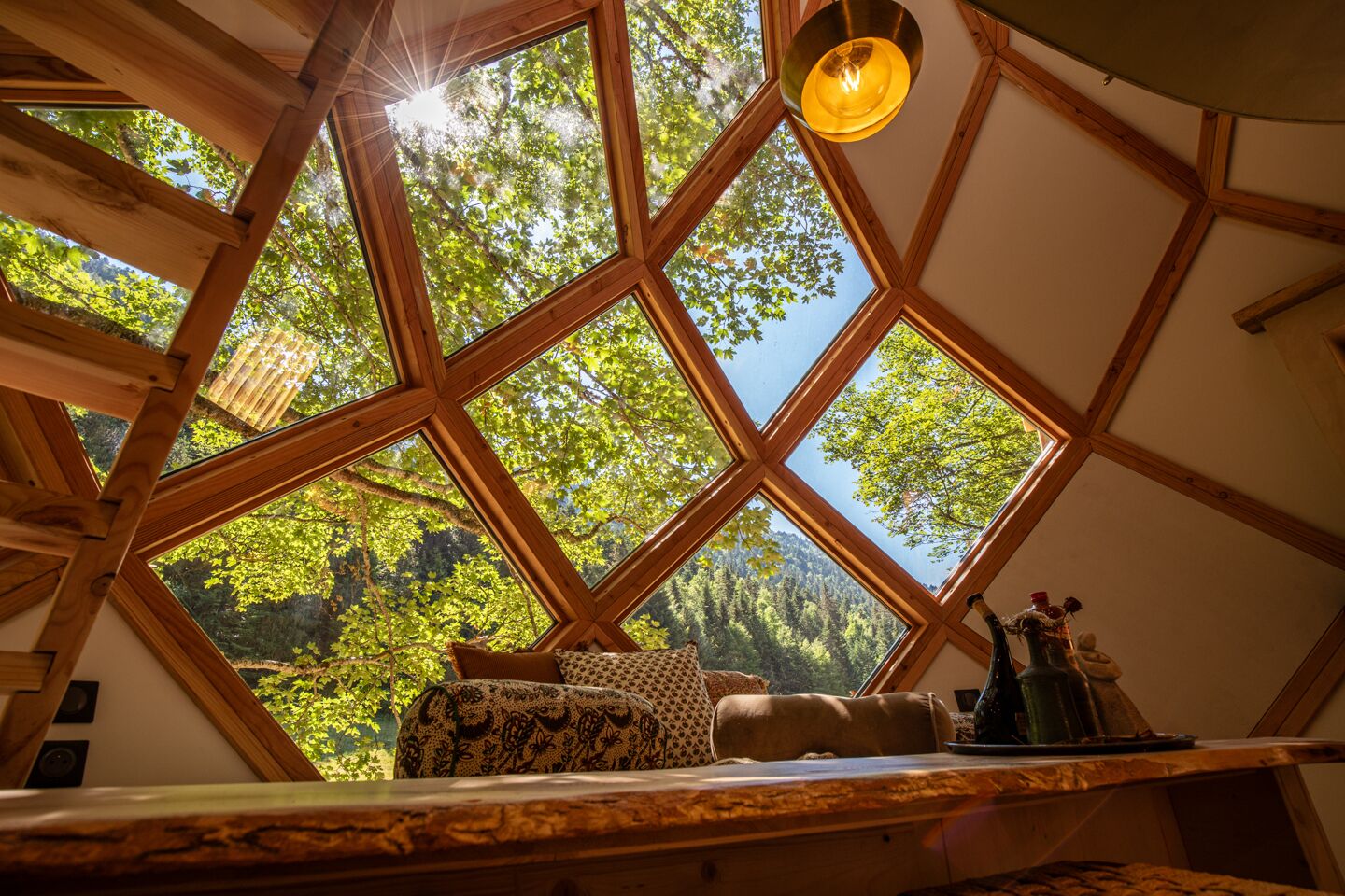 Une pièce avec un plafond en bois et de grandes fenêtres, un canapé agrémenté de coussins à motifs et une petite table ornée d’objets décoratifs.