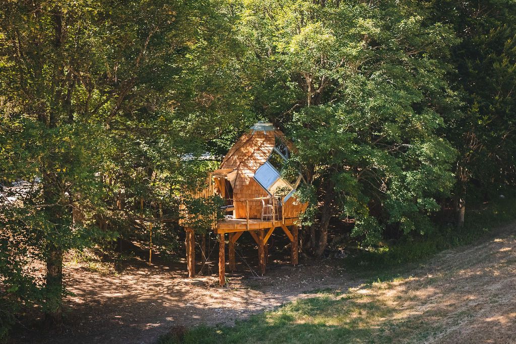 Une cabane perchée dans les arbres, construite sur pilotis, entourée d’une forêt dense.