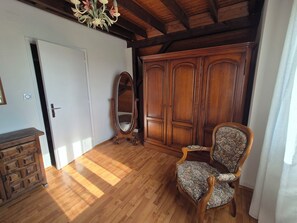 A room with wooden flooring, a wardrobe, a chair, and a mirror. - Charmante maison à Sundhoffen classée 3 clés parfaite pour des séjours reposants (sundhoffen)
