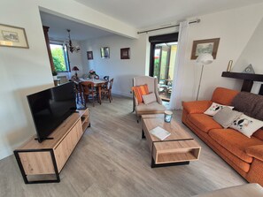 Una sala de estar con televisor, muebles de madera, un sofá y un comedor con mesa y sillas.