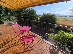 A balcony with a view of a field and mountains, featuring a table and chairs. - Charmante maison à Sundhoffen classée 3 clés parfaite pour des séjours reposants (sundhoffen)
