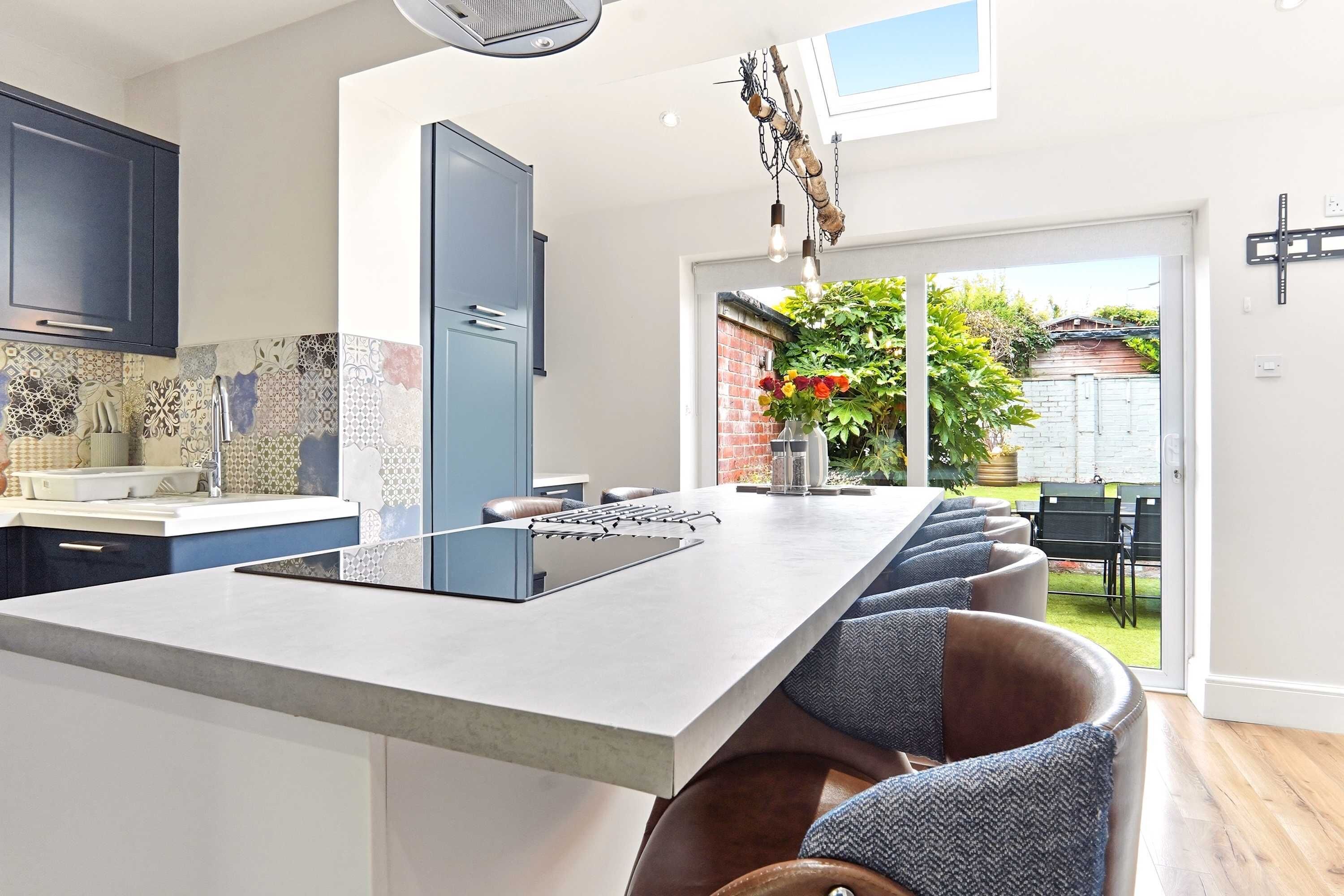A modern kitchen with a large island, a built-in oven, and a view of the garden through the sliding glass door.