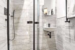 Ein modernes Badezimmer mit einer Duschkabine aus Glas, einem Waschbecken mit Marmorplatte und einem Spiegel darüber.