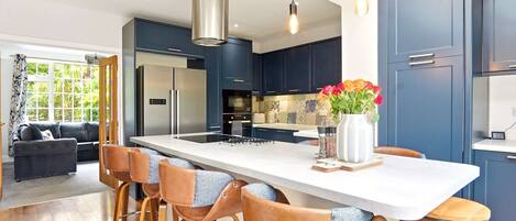 A modern kitchen with a central island, bar stools, and a dining area with a sofa.