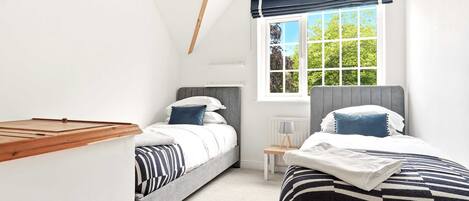 A bedroom with two beds, a window with a view of trees, and a small bedside table with a lamp.