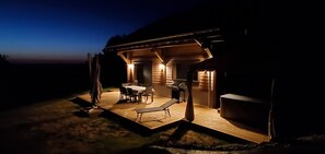 Eine Holzhütte mit einer Terrasse, Sitzgelegenheiten im Freien und einer Grillstelle.