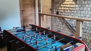 A wooden-floored room with a foosball table, wooden beams, and a brick wall.