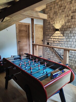A wooden-floored room with a foosball table, wooden beams, and a brick wall. - Sublime chalet au coeur des montagnes vosgiennes - 3 chambres, Sauna, Jacuzzi (Anould)