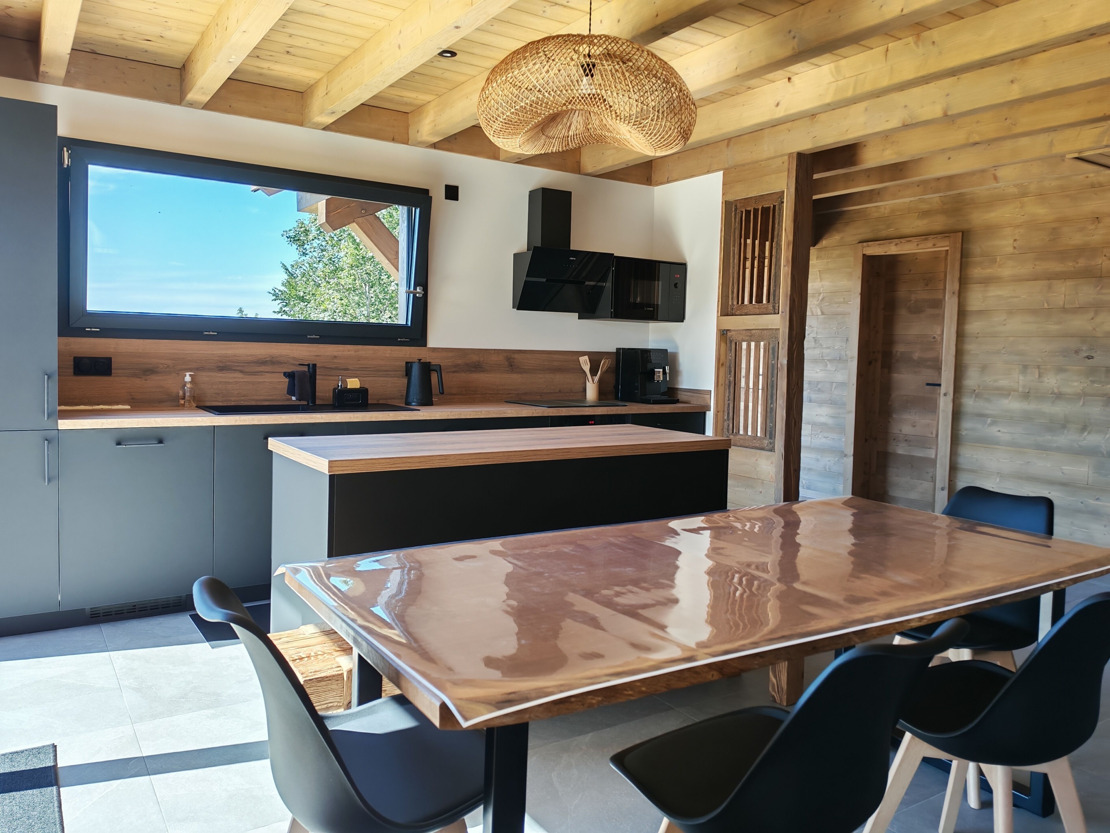 A modern kitchen with a wooden ceiling, a large island, and a dining area with chairs.