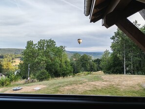 A view from inside a vehicle, overlooking a grassy area with trees and a distant hot air balloon. - Sublime chalet au coeur des montagnes vosgiennes - 3 chambres, Sauna, Jacuzzi (Anould)