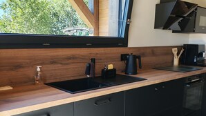 A modern kitchen with a wooden countertop, black cabinets, a black sink, and a window overlooking greenery.