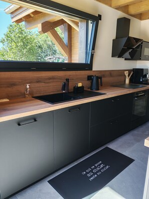A modern kitchen with a wooden countertop, black cabinets, a black sink, and a window overlooking greenery. - Sublime chalet au coeur des montagnes vosgiennes - 3 chambres, Sauna, Jacuzzi (Anould)