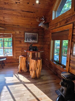 A wooden cabin interior with a dining table, chairs, and a mounted deer head.