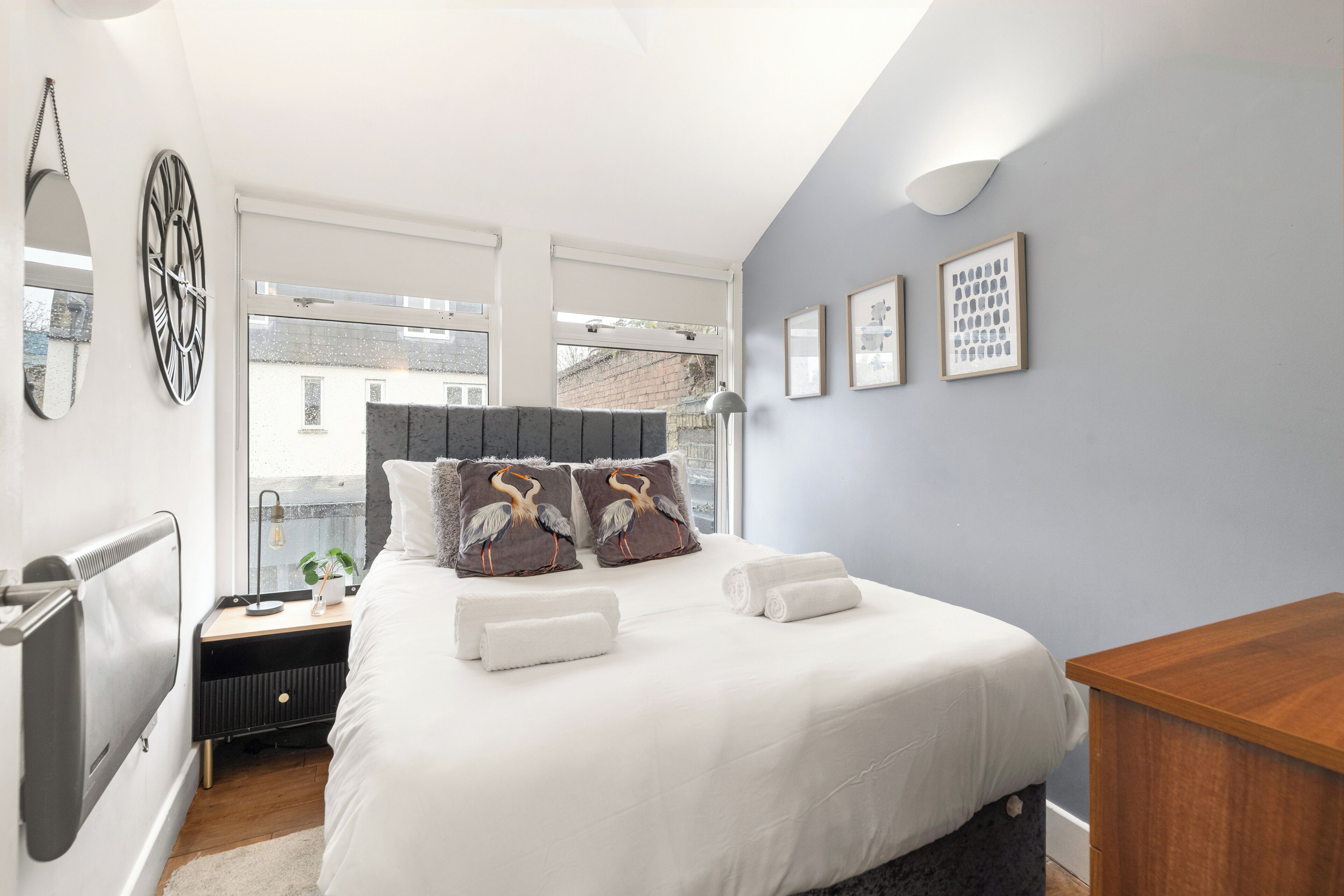 A modern bedroom with a large bed, two pillows, a bedside table, a lamp, and a view of the outside.
