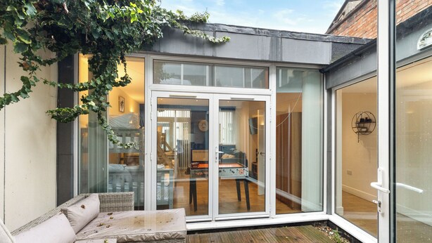 A modern patio with glass doors leading to an interior space, wicker furniture, and a visible staircase. - Exquisite 4BR Home 15 Guests Prime Central London (London)