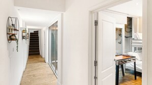 A hallway with a wooden floor, a staircase, and a bed with a table in the adjacent room. - Exquisite 4BR Home 15 Guests Prime Central London (London)