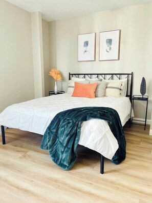 Ein Schlafzimmer mit einem Bett, Kissen, einem Nachttisch und einem an der Wand hängenden Bilderrahmen.
