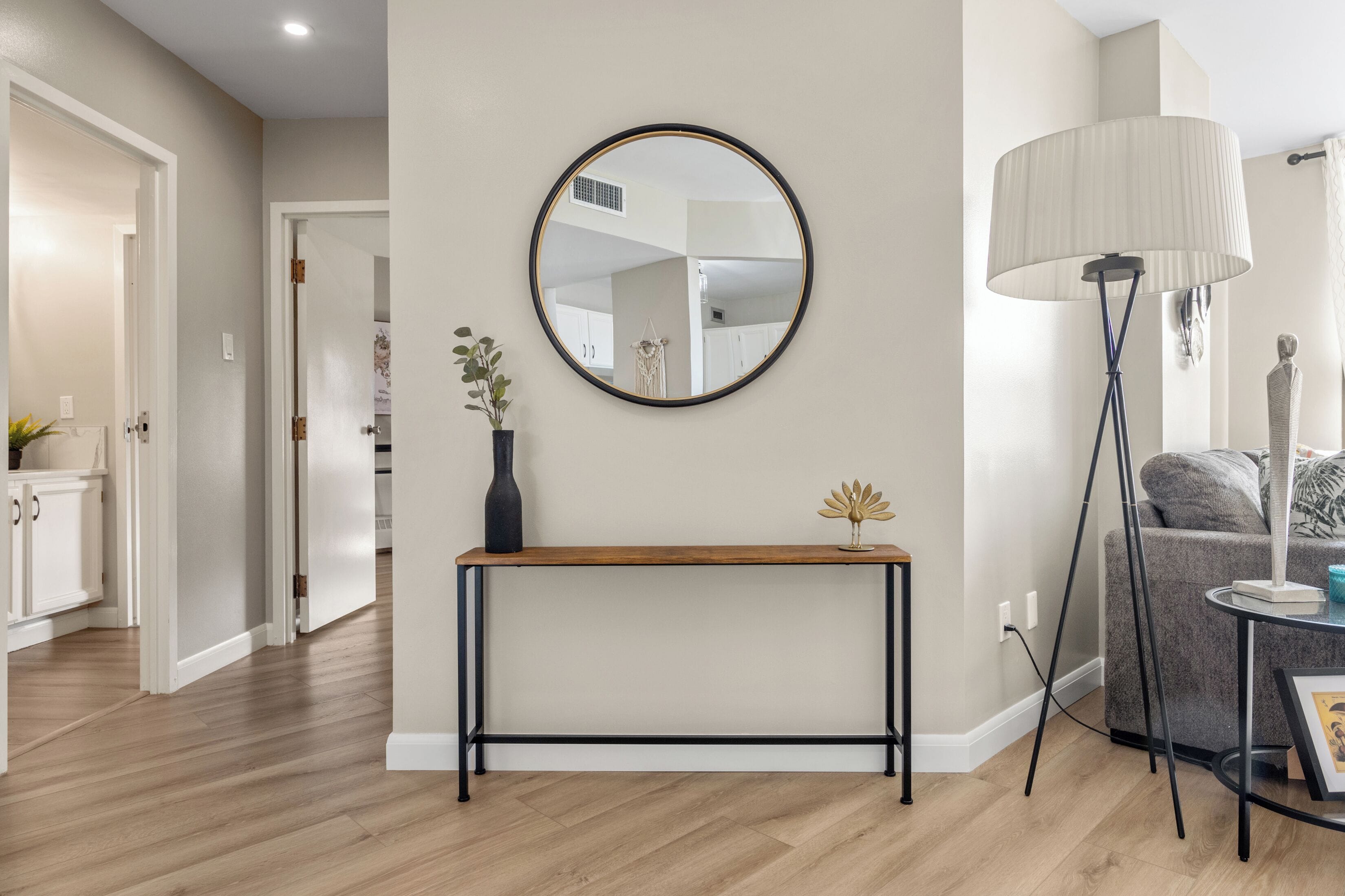 Un salon moderne avec un grand miroir rond, une console, une lampe sur pied et un canapé gris.