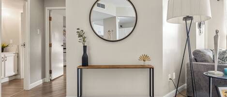 Un salon moderne avec un grand miroir rond, une console, une lampe sur pied et un canapé gris.