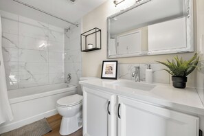 Et badeværelse med badekar, toilet, vaskebord med spejl og en potteplante.