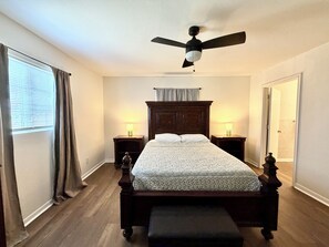 A bedroom with a bed, two bedside tables, a ceiling fan, and a window with curtains.