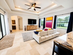 A modern living room with a sofa, television, and a ceiling fan. - Spacious 5-bedroom Luxury Courtyard Estate in ALVA Pool + Resort Style Amenities (Alva)