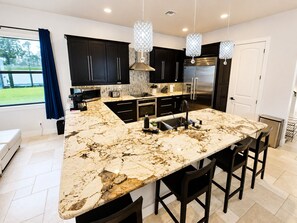 A modern kitchen with a large island, dark cabinetry, stainless steel appliances, and pendant lighting. - Spacious 5-bedroom Luxury Courtyard Estate in ALVA Pool + Resort Style Amenities (Alva)