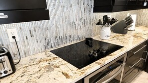 Een keuken met een zwart inductiekookplaatje, een marmeren aanrechtblad en roestvrijstalen apparatuur.