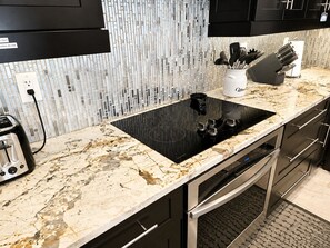 A kitchen with a black induction cooktop, a marble countertop, and stainless steel appliances. - Spacious 5-bedroom Luxury Courtyard Estate in ALVA Pool + Resort Style Amenities (Alva)