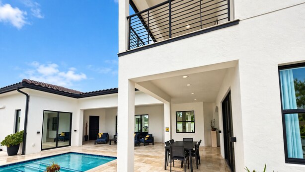 Een modern huis met twee verdiepingen, een zwembad, buitenmeubilair en een overdekte patio.