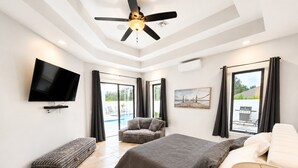 Een moderne slaapkamer met een bed, een flatscreen televisie, een plafondventilator en uitzicht op de omgeving.