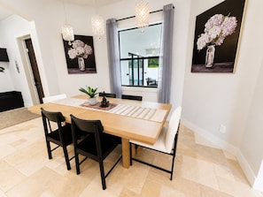 A dining area with a wooden table, black chairs, a potted plant, and artwork on the walls. - Spacious 5-bedroom Luxury Courtyard Estate in ALVA Pool + Resort Style Amenities (Alva)