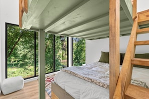 Ein Schlafzimmer mit großem Fenster, einer Holzleiter und einem Bett mit gemusterten Betttextilien.
