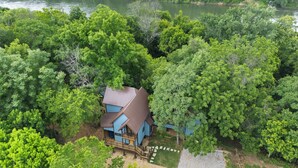 A house surrounded by dense forest, with a clear view of the river in the background. - Luxury Treehouse on 470 Acre Adventure on Two Rivers (Mountain View)