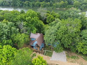 A house surrounded by dense forest, with a clear view of the river in the background. - Luxury Treehouse on 470 Acre Adventure on Two Rivers (Mountain View)