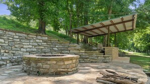 A stone fire pit area with a wooden bench and a covered seating area. - Luxury Treehouse on 470 Acre Adventure on Two Rivers (Mountain View)