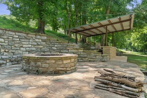 A stone fire pit area with a wooden bench and a covered seating area. - Luxury Treehouse on 470 Acre Adventure on Two Rivers (Mountain View)