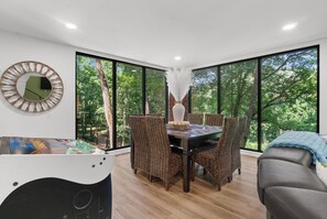 Un coin repas avec une table en bois, des chaises en osier et une grande fenêtre donnant sur la forêt.
