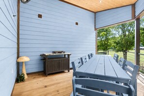 Ein überdachter Essbereich im Freien mit einem langen Tisch, Bänken, einem Grill und einer kleinen Lampe.