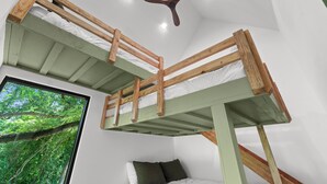 A bunk bed room with a ceiling fan, a window with a view of trees, and a bed with pillows. - Luxury Treehouse on 470 Acre Adventure on Two Rivers (Mountain View)