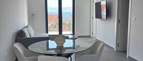 Un moderno comedor con una mesa de vidrio y cuatro sillas, un sofá, y un televisor montado en la pared.