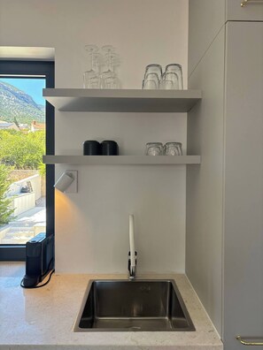Eine Küche mit integriertem Spülbecken, oberen Regalen mit Gläsern und Blick auf eine gebirgige Landschaft durch ein Fenster.
