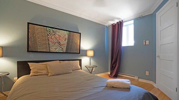 A bedroom with a bed, a nightstand, a lamp, a window with curtains, and a door. - Designer 3BR • Two Levels • 2.5 BTHR (Montréal)