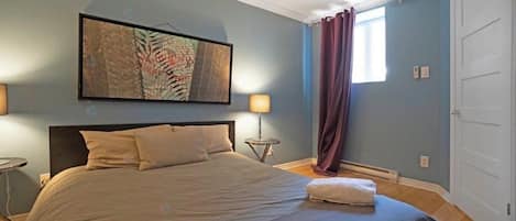 Une chambre à coucher avec un lit, une table de chevet, une lampe, une fenêtre avec des rideaux et une porte.