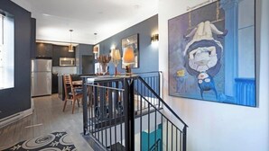 A modern kitchen with stainless steel appliances, a dining area with wooden chairs, and a staircase with a black railing. - Designer 3BR • Two Levels • 2.5 BTHR (Montréal)