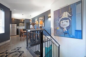 A modern kitchen with stainless steel appliances, a dining area with wooden chairs, and a staircase with a black railing. - Designer 3BR • Two Levels • 2.5 BTHR (Montréal)