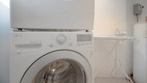 A white washing machine with a control panel, a transparent water tank, and a power outlet on the wall. - Designer 3BR • Two Levels • 2.5 BTHR (Montréal)