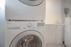 A white washing machine with a control panel, a transparent water tank, and a power outlet on the wall. - Designer 3BR • Two Levels • 2.5 BTHR (Montréal)