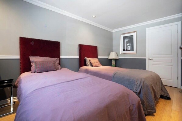 Une chambre d’hôtel avec deux lits, une porte, une table de chevet avec une lampe et un tableau encadré au mur.