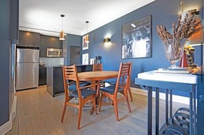 Une cuisine moderne avec un coin repas, comprenant un réfrigérateur en acier inoxydable, un four à micro-ondes et une table à manger en bois avec des chaises.